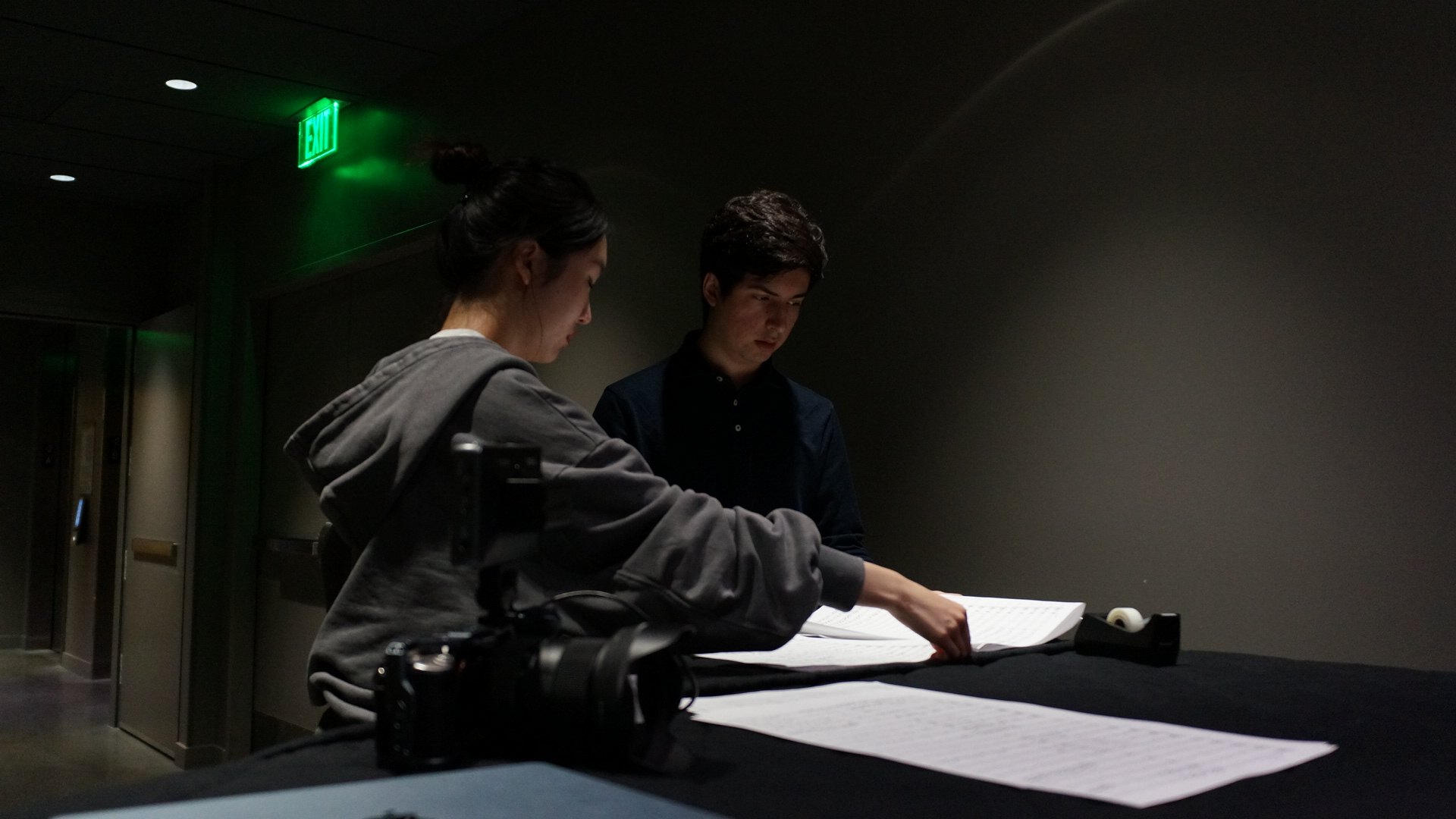 Two film team members reviewing music and camera materials before an orchestral recording session